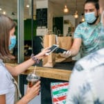 Young woman with mask paying with mobile a take away order